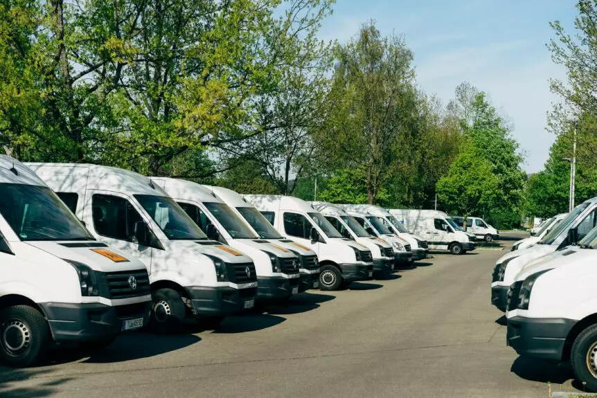 Diagonal view of a parking lot surrounded by trees, filled with rows of white cargo vans