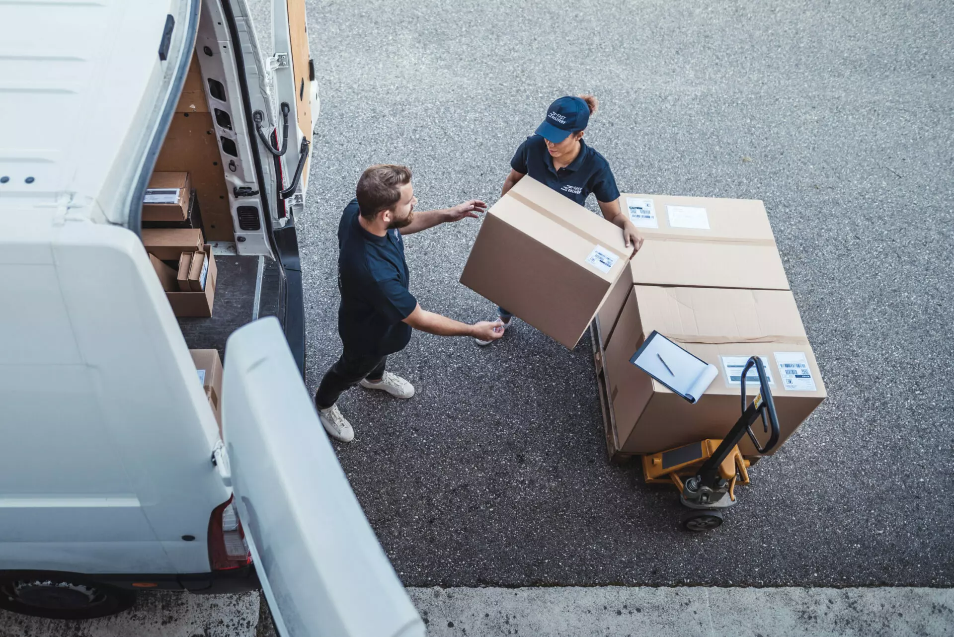 a man and a woman loading packages from a dolly into a white cargo delivery van