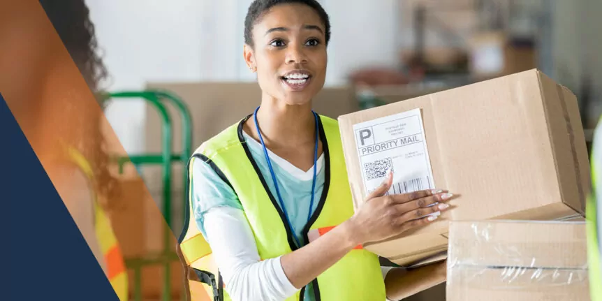 a woman in a yellow vest holding a box with a priority mail label on it inside a warehouse