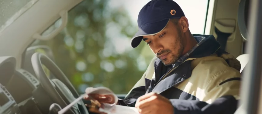 An ExpressIt Delivery man, wearing a cap with a log on it, checking his package list in a vehicle